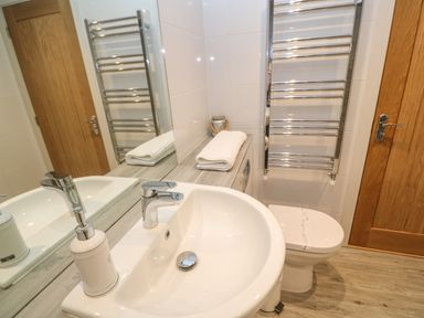 A bathroom with a sink a towel on a countertop a toilet a heated towel rail and a wooden door at Seafield in Carbis Bay near St Ives