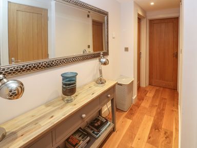 A hallway with wooden floor wooden doors a console table with lamps a vase a large mirror and a laundry basket at Seafield in Carbis Bay near St Ives