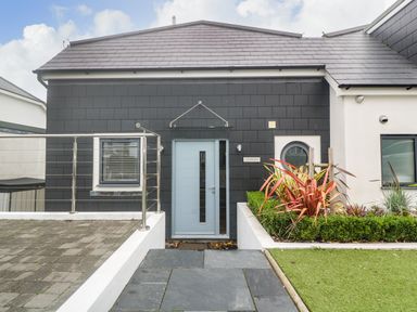 The front entrance of a modern house with a blue door gray shingles a small window and a garden bed with plants at Seafield Carbis Bay near St Ives