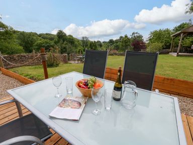 An outdoor dining area with a table set with glasses and fruits at Mallows Byre in Yetminster