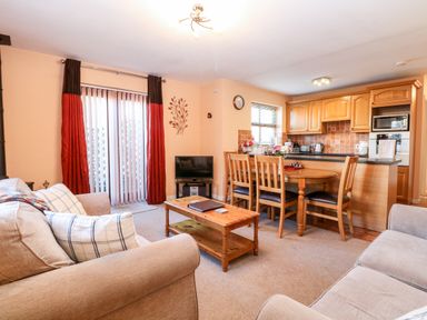 A living room with a beige sofa coffee table dining table and kitchen area at The Ramblers Annex in Mattishall