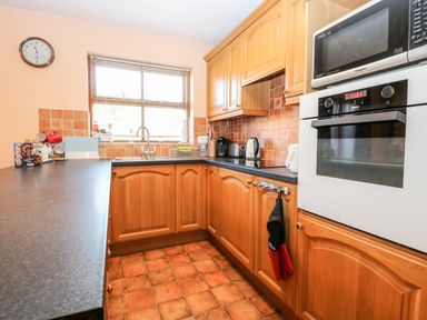 A kitchen with wooden cabinets black countertops a stove microwave and a window at The Ramblers Annex in Mattishall
