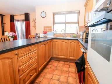 A kitchen with wooden cabinets black countertops a sink window with blinds and a clock on the wall at The Ramblers' Annex in Mattishall