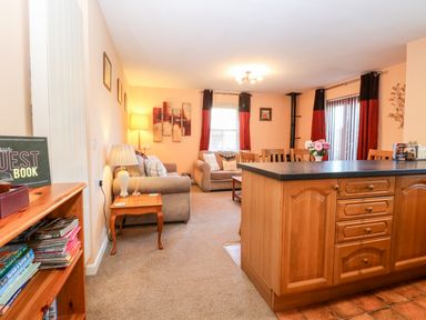 An open living and dining room with sofas a wooden dining table wooden cabinets and curtains at The Ramblers Annex in Mattishall