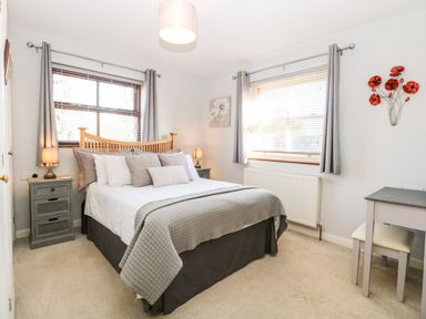 A bedroom with a double bed grey bedside tables and lamps two windows and a small desk with a chair at The Ramblers Annex in Mattishall