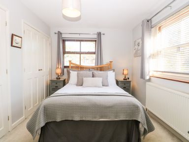 A bedroom with a bed between two bedside tables and windows with curtains at The Ramblers Annex in Mattishall