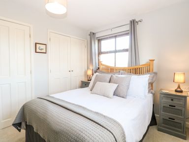 A bedroom with a wooden bed frame white and gray bedding two nightstands with lamps and a window with gray curtains at The Ramblers Annex in Mattishall