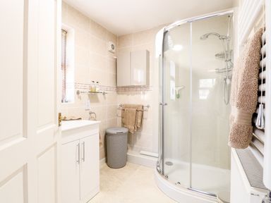 A bathroom with a curved glass shower, white sink cabinet, towel racks with towels, and a laundry basket at The Ramblers Annex in Mattishall