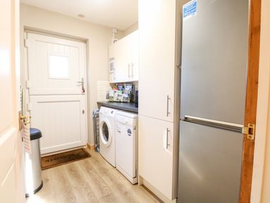 A utility room with a white washing machine, dishwasher, tall white cabinets, and a stainless steel fridge freezer at The Ramblers Annex in Mattishall