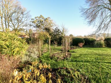 A garden with grass lawn bushes trees and wooden trellis structures at The Ramblers Annex in Mattishall