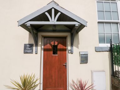 A wooden door with a small window under a gray porch roof with a sign reading The Old Chapel and a mailbox on the wall at Old Chapel in Cloughton