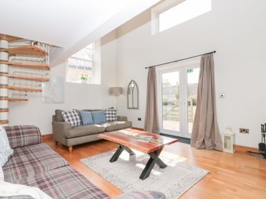 A living room with sofas a wooden coffee table a spiral staircase and French doors at Old Chapel in Cloughton