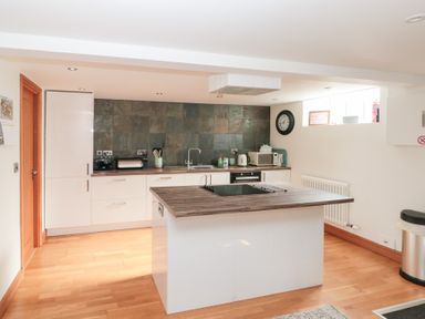 A kitchen with wooden floor white cabinetry a central island with stove and a tiled backsplash at Old Chapel in Cloughton