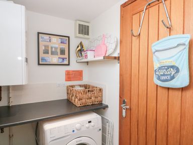 A laundry room with a washing machine basket and cleaning items on a shelf and a wooden door with a laundry service bag at Old Chapel in Cloughton