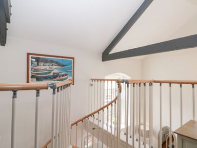 A stair railing with wooden handrails and white balusters under a ceiling with visible beams and a painting of boats on the wall at Old Chapel in Cloughton