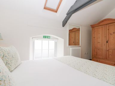 A bedroom with a bed, wooden wardrobe, radiator, mirror, skylight, and window at Old Chapel in Cloughton