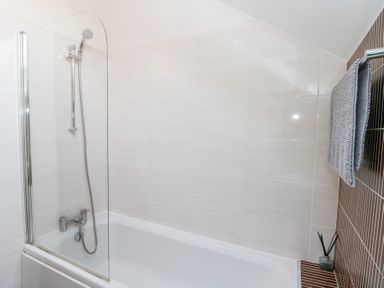 A bathroom with a bathtub shower combination glass shower screen a towel hanging on the wall and a reed diffuser on a tiled surface at Old Chapel in Cloughton