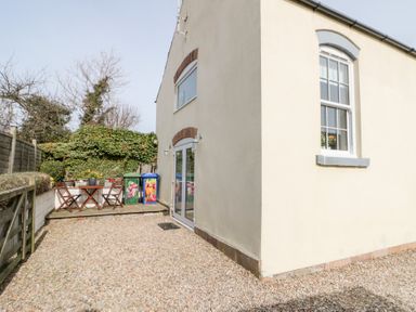 Exterior side of a cream house with gravel ground and wooden fence with a small patio table and chairs at Old Chapel in Cloughton