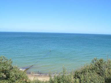 A beach with people near the shore and a view of the ocean with vegetation in the foreground at 20 Siesta Mar in Mundesley