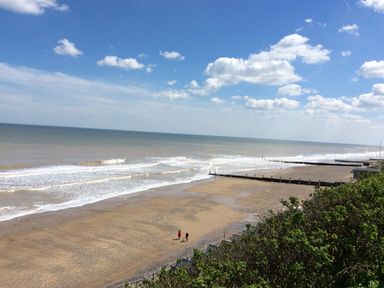 A sandy beach with small waves and three people walking near the water at 20 Siesta Mar in Mundesley