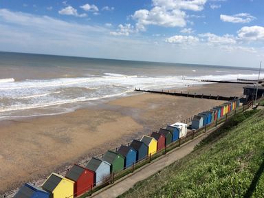 A beach with colorful beach huts along a path near the sea at 20 Siesta Mar in Mundesley
