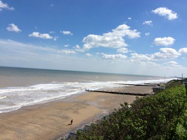 A sandy beach with wooden groynes and a person walking near the shore at 20 Siesta Mar in Mundesley