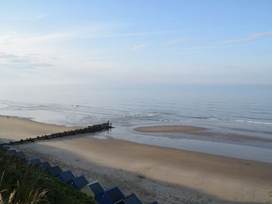 A beach with colorful huts along the shore and a wooden groyne extending into the sea at 20 Siesta Mar in Mundesley