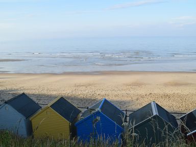A sandy beach with small colorful beach huts along the shore at 20 Siesta Mar in Mundesley