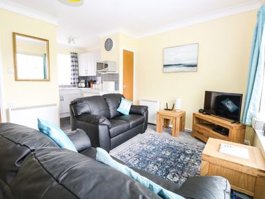 A living room with black leather sofas a blue patterned rug wooden furniture and a television at 20 Siesta Mar in Mundesley
