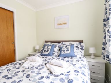 A bedroom with a bed covered in blue leaf patterned bedding bedside tables with lamps and a wooden door at 20 Siesta Mar in Mundesley