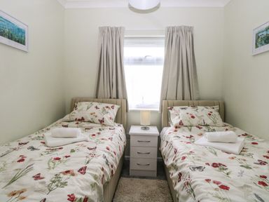 A bedroom with two single beds with floral bedding a bedside table with a lamp and a window with curtains at 20 Siesta Mar in Mundesley