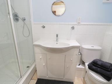 A bathroom with a shower cubicle sink cabinet round mirror and toilet with folded towels at The Annex @ Garden House in Prudhoe near Newcastle