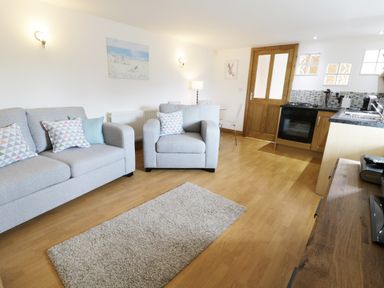 A living room with grey sofa and armchair near a kitchen with wooden cabinets at The Annex @ Garden House in Prudhoe near Newcastle