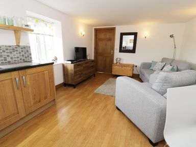 A living room with a gray sofa a wooden cabinet a wooden door and a kitchen area at The Annex @ Garden House Prudhoe near Newcastle
