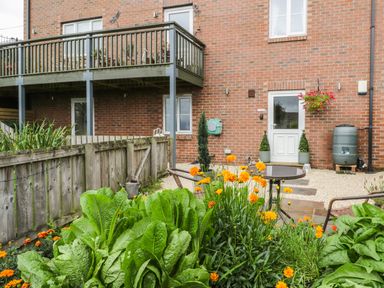 A garden with green plants and orange flowers in front of a brick building with a balcony and a white door at The Annex @ Garden House Prudhoe near Newcastle