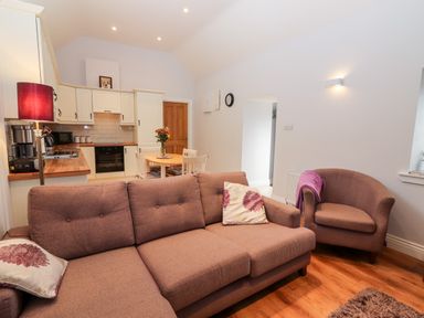 An open living room and kitchen with a brown sofa, armchair, round dining table, and kitchen cabinets at Laharn Cottage in Killorglin County Kerry