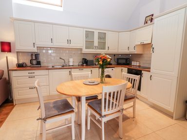 A kitchen with white cabinets a wooden dining table with chairs and flowers at Laharn Cottage in Killorglin County Kerry