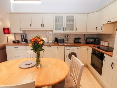 A kitchen with cream cabinets wooden countertops a round wooden table with flowers and chairs at Laharn Cottage in Killorglin County Kerry