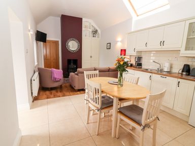 A kitchen and dining area with a wooden table and four chairs next to a living room with sofas and a fireplace at Laharn Cottage in Killorglin County Kerry