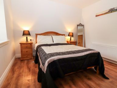 A bedroom with a wooden bed and two bedside tables with lamps and a standing mirror at Laharn Cottage in Killorglin County Kerry