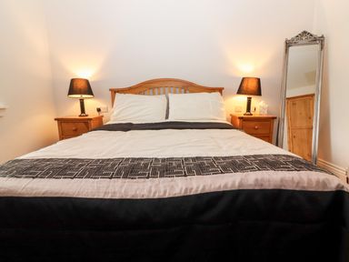 A bedroom with a wooden bed and two bedside tables with lamps and a standing mirror at Laharn Cottage in Killorglin County Kerry