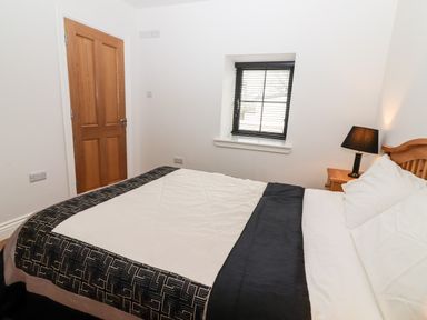 A bedroom with a bed a wooden door a window and a bedside table with a lamp at Laharn Cottage in Killorglin County Kerry