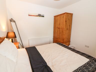 A bedroom with a bed a wooden wardrobe a standing mirror and a bedside lamp at Laharn Cottage in Killorglin County Kerry