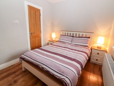 A bedroom with a double bed striped bedding two bedside tables with lamps and a wooden door at Laharn Cottage in Killorglin County Kerry