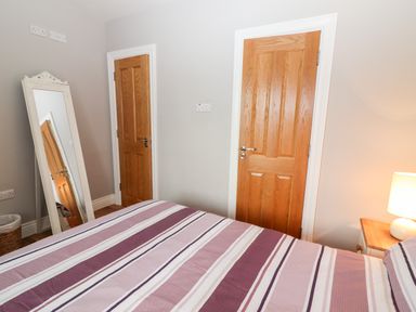 A bedroom with a striped bedspread a free standing mirror two wooden doors and a bedside table with a lamp at Laharn Cottage in Killorglin County Kerry