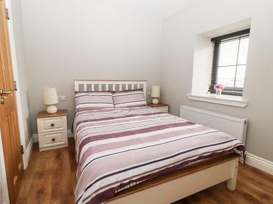A bedroom with a double bed striped bedding two bedside tables with lamps a window with blinds and flowers at Laharn Cottage in Killorglin County Kerry