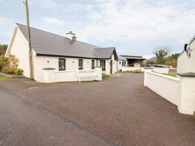 A single story cottage with a paved driveway and a white bench labeled Laharn Cottage at Laharn Cottage in Killorglin County Kerry