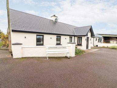 A white cottage building with a tiled roof and a white bench outside in Killorglin County Kerry