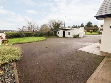 A paved driveway area with a small white outbuilding green grass and bushes at Laharn Cottage in Killorglin County Kerry