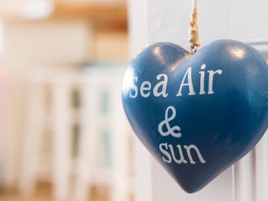 A blue heart-shaped hanging decoration with the words Sea Air and Sun on a white door